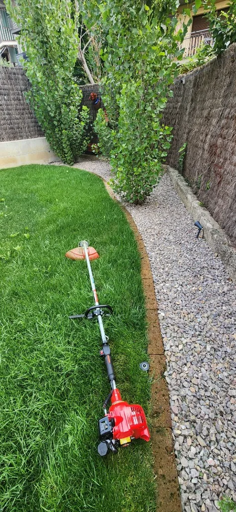 Desbrossament de vores de gespa amb desbrossadora al costat de camí de grava a Osona