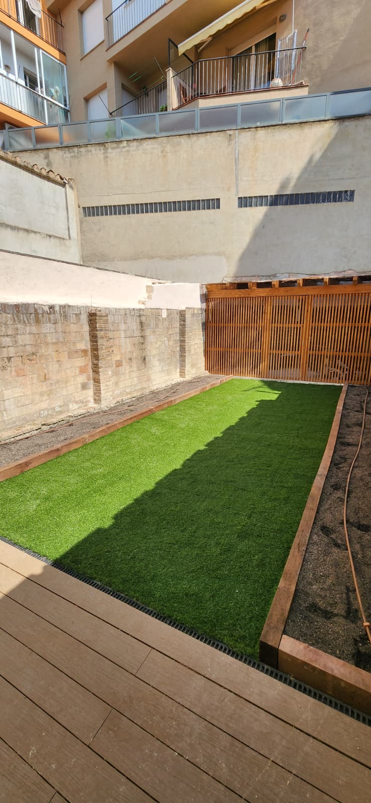 Pati amb gespa artificial i travesses de fusta a Osona