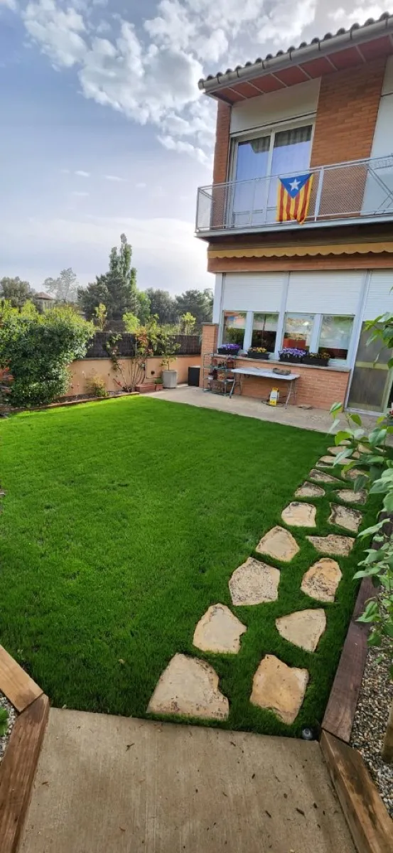 Jardí amb gespa artificial i camí de pedra natural a Osona