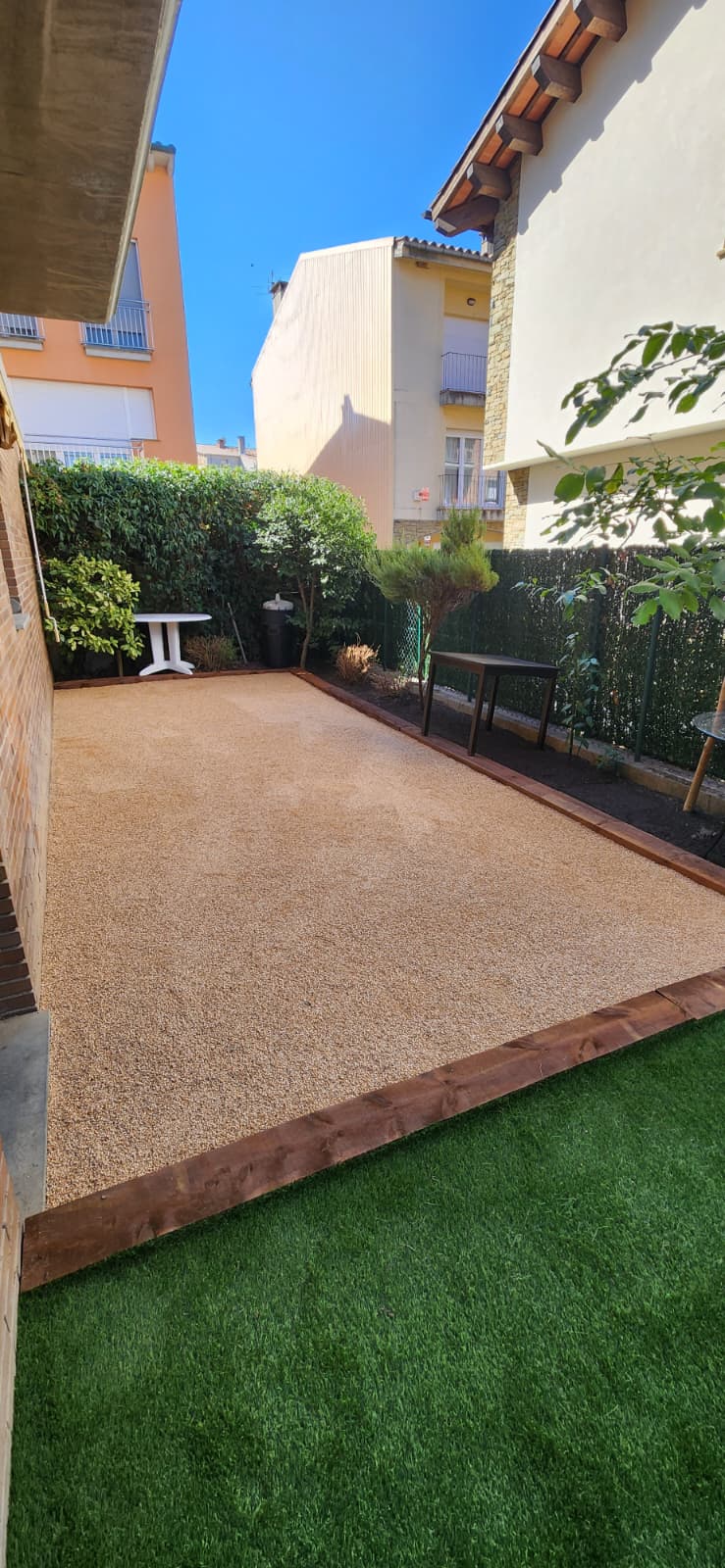 Jardí amb grava decorativa, travesses de fusta i gespa artificial a Osona