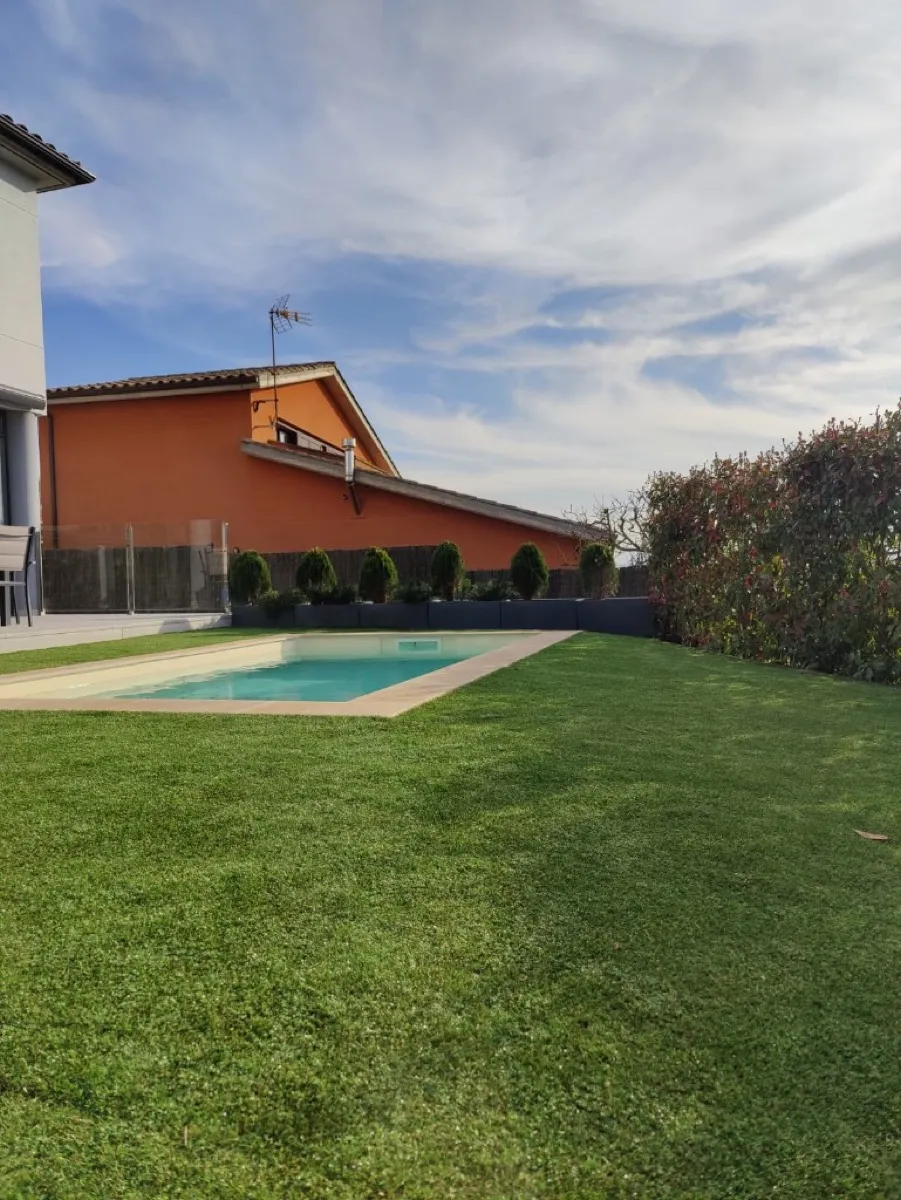 Jardí amb gespa artificial i jardineres al voltant de piscina a Vic